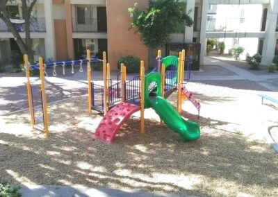Small colorful commercial playground with a green slide in a shaded courtyard