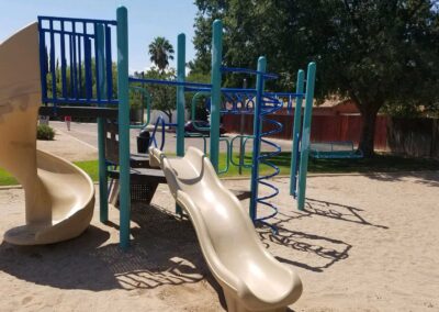 Tan spiral slide and blue climbing bars on a sand play surface