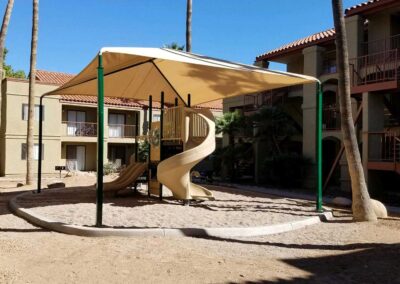 Shade sail over a tan spiral slide structure at an apartment complex