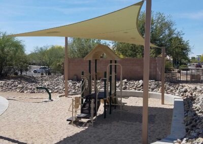 Tan shade sail over a small commercial play structure in a gravel play area