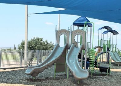 Shade sail over a gray commercial playground with twin slides