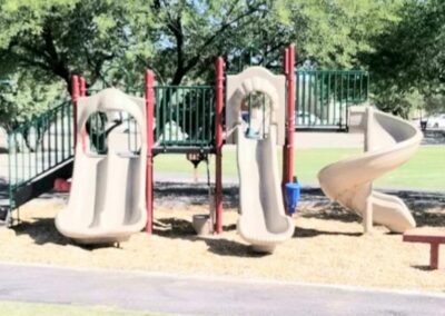 Gray and red commercial play structure with slides on a park lawn