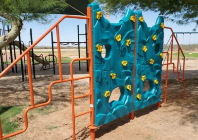 Orange climbing bars and a teal rock wall on a commercial playground