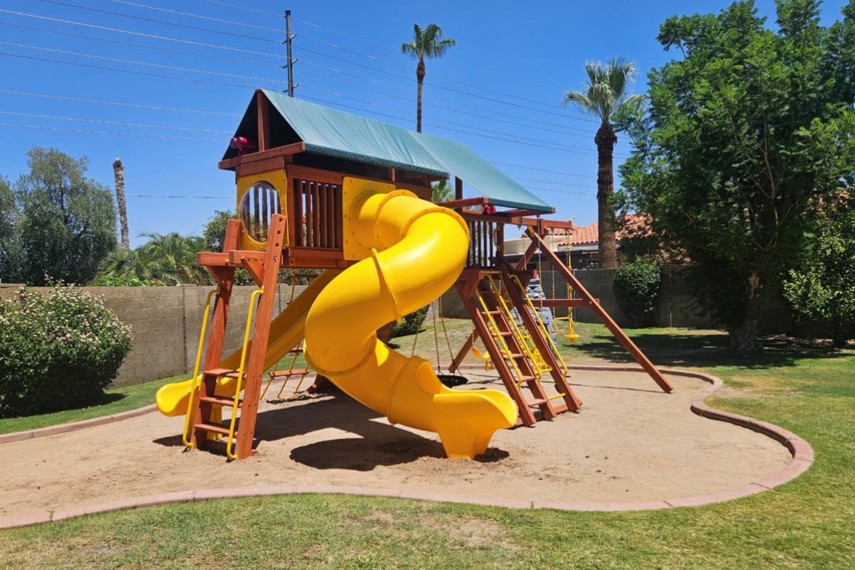 Cedar playset with a canopy roof shading the deck and slide in a Tucson backyard